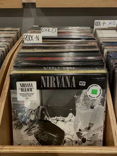 several records are stacked on top of each other in a record store display case with labels reading nirvana