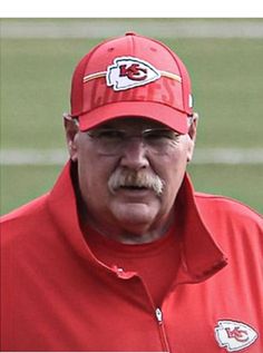 a man with a mustache wearing a red kansas chiefs baseball cap and glasses on the field