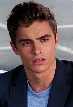 a young man in a blue shirt and blazer looking at the camera with an angry look on his face