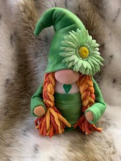 a stuffed toy with a green hat and flower on it's head sitting on a fur surface