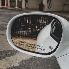 a side view mirror on the back of a white car with writing on it that reads, your demons are closer than they appear