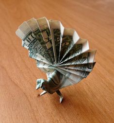 an origami bird made out of one hundred dollar bills on a wooden table