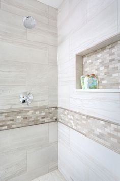 a white tiled shower with two faucets on the wall and shelves above it