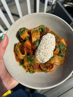 a person is holding a bowl of pasta with sauce and broccoli on top