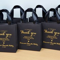 black bags with gold foil lettering and thank you written on the handles are lined up against a wooden table