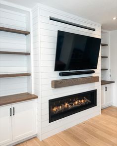 a flat screen tv mounted on the wall above a fireplace in a room with white walls