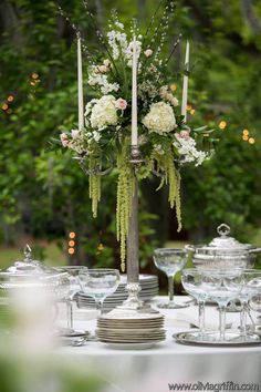 a tall silver candelabra filled with white flowers and greenery on top of a table