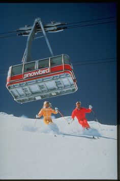 two people riding skis on top of a snow covered slope under a ski lift