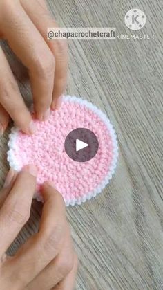 two hands are holding a crocheted pink and white object on a wooden table