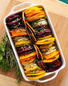 roasted beets and carrots in a casserole dish with herbs on the side