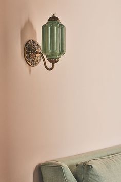 a green light fixture mounted to the side of a pink wall next to a couch