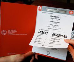 a person holding up a menu in front of a red folder with writing on it