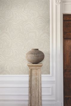 a vase sitting on top of a pedestal in front of a wallpapered room