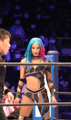 a woman with blue hair standing next to a man in a wrestling ring at night