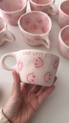 a hand holding a pink coffee cup in front of many cups with hearts on them