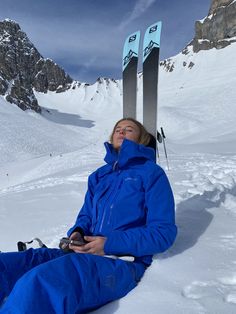 a woman sitting in the snow with skis on her head and legs resting next to her