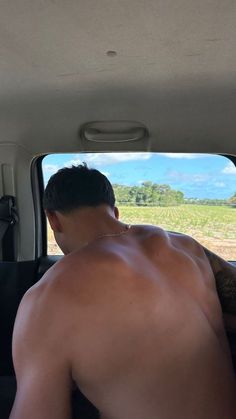 a shirtless man sitting in the back seat of a car looking out at an open field