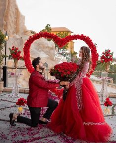 a man kneeling down next to a woman in a red dress and holding a bouquet