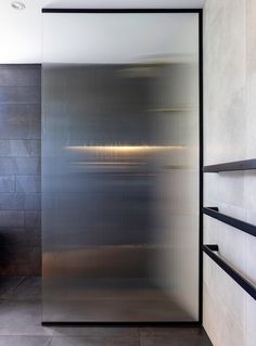 a bathroom with a glass shower door and tiled walls, along with shelves on the wall