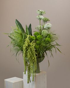 a white vase with green plants in it on a table next to two cubes