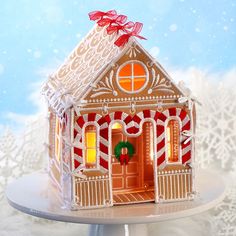 a small gingerbread house with a red bow on the front door and snow covered trees in the background