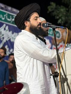 a man standing in front of a microphone on top of a white table next to a crowd