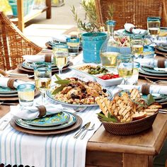 a table set with plates, glasses and food on it for an outdoor dinner party