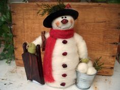 a snowman with a red scarf and hat is next to a bucket of balls