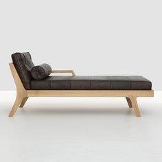 a black leather chaise lounger with wooden legs and back rests against a white wall