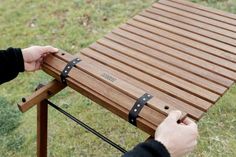 a person holding onto a wooden bench with leather straps on it's sides and another hand reaching for the slats