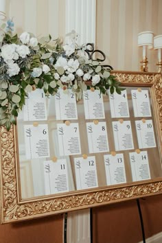 a gold framed calendar with white flowers and greenery