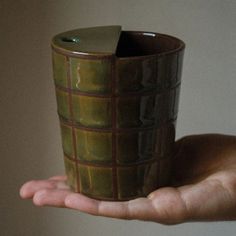 a hand holding a green ceramic cup in it's palm