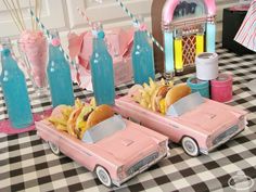 two pink toy cars with hot dogs and french fries in them on a checkered tablecloth