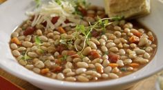 a white bowl filled with beans next to a piece of bread on top of a wooden cutting board