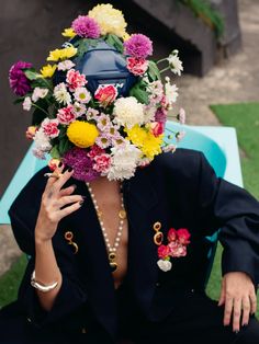 a woman sitting on top of a blue bench with flowers in her hair and necklaces around her neck