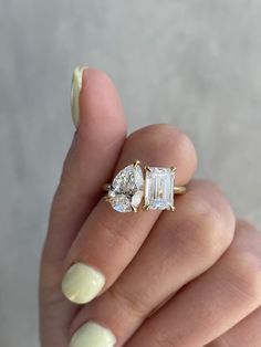 a woman's hand holding an engagement ring with two pear shaped diamonds