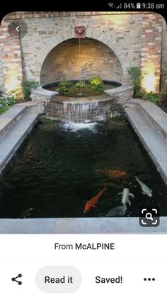 a fish pond in the middle of a brick wall with a waterfall coming out of it