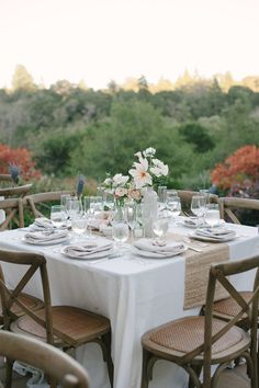 the table is set with plates, glasses and flowers in vases on top of it