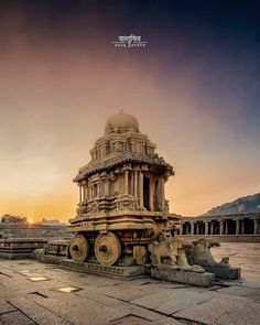 the sun is setting over an old building with wheels and pillars in front of it