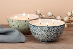 two tea lights sitting on top of a wooden table next to a blue and white bowl