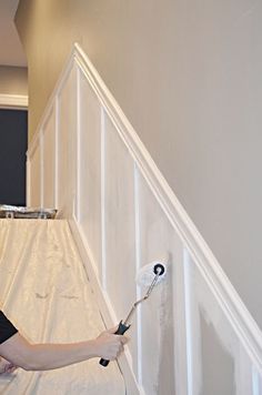 a woman is painting the wall with rollers and paintbrushes in her hand