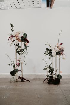 three tall vases with flowers and greenery in them on the floor next to a wall