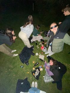 a group of people sitting on the grass with food and drinks in their hands at night