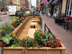 a row of wooden benches sitting on top of a sidewalk next to tables and chairs