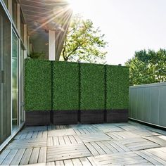 an outdoor patio with wooden flooring and green privacy screens on the side of it