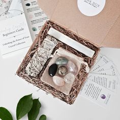 an open box with various items inside on top of a white table next to some green leaves