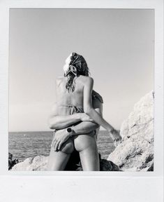 a woman sitting on top of a rock next to the ocean with her arms crossed