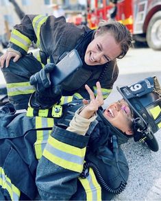 two fire fighters giving the peace sign to each other while sitting on the ground in front of a firetruck