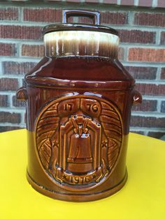 a brown jar sitting on top of a table next to a brick wall and yellow table