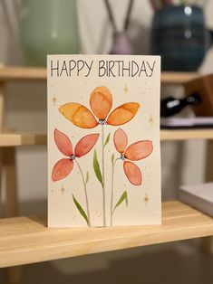 a happy birthday card with watercolor flowers and stars on the front, sitting on a table